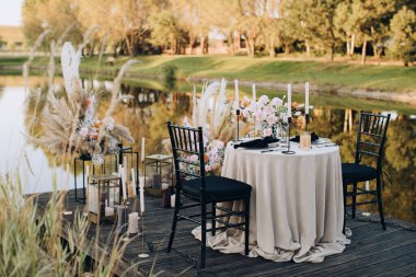 Açık hava düğün masasında, göl kıyısında boho tarzında çiçeklerle süslenmiş.