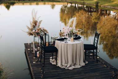 Gün batımında göl kenarında iki kişilik romantik bir akşam yemeği.