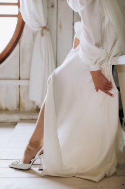 Beyaz elbiseli gelin otelde ayakkabı giyiyor. Gelinin sabahı