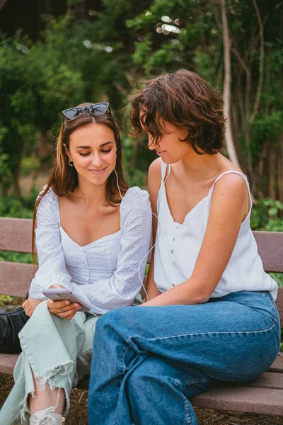 Dva Dospívající Přátelé Dívají Telefon Poslouchají Hudbu Zatímco Sedí Lavičce — Stock fotografie