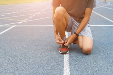 Stadyumdaki mavi koşu pistindeki sporcunun yakın çekimi. Antrenmandan önce spor ayakkabılarını spor ayakkabılarına bağlıyor. Çalışan konsept.