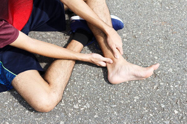 Sport man holding ankle in pain due to sprained ankle. Injury from workout concept