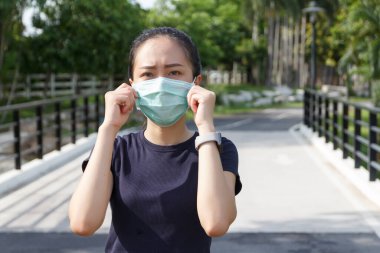 Tıbbi koruyucu maskeli genç kadın parkta dinleniyor. COVID19 'dan koruyucu maske kullanma kampanyası