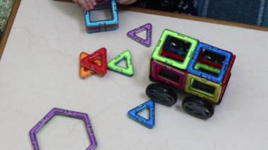 Kız masanın üzerindeki manyetik yapıcının parçalarından makinenin bir heykelini yapıyor. Yapıcı ile eğitici oyunlar.