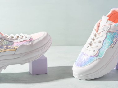 Turkuaz arka planda geometrik podyumlarda pulları olan beyaz pastel spor ayakkabılar.