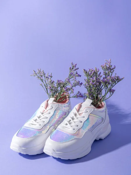 White female sneakers with sequins with flowers inside on purple background, spring summer fashion concept, vertical