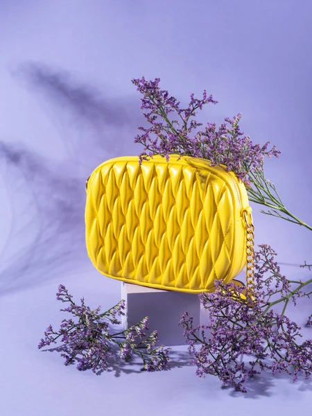 Yellow fashion lady handbag purse with flowers on purple background and geometric podium, spring summer fashion concept