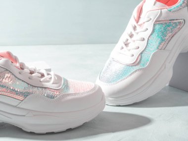 Turkuaz arka planda geometrik podyumlarda pulları olan beyaz pastel spor ayakkabılar.