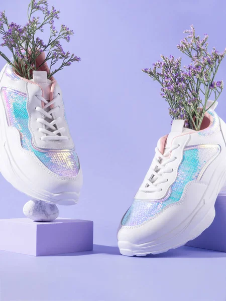 White female sneakers with sequins with flowers inside on purple background with geometric cube podium, spring summer fashion balance concept