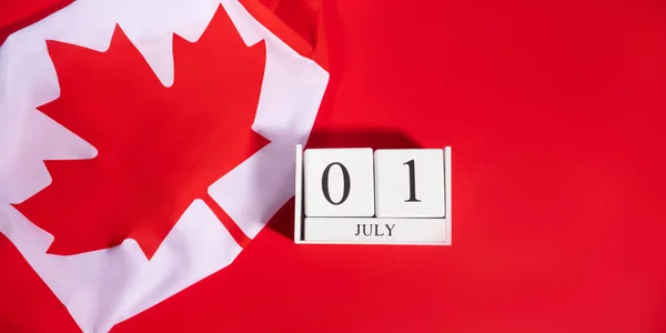 加拿大日概念与加拿大国旗碎片和7月1日日期在白色木制日历上的黑体字红色背景 平铺横幅 — 图库照片