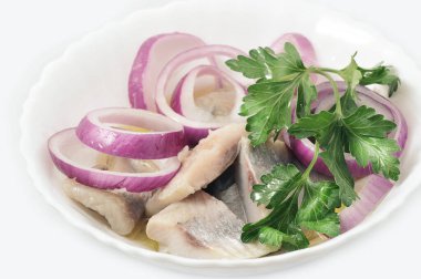herring in white dish with red onion and parsley