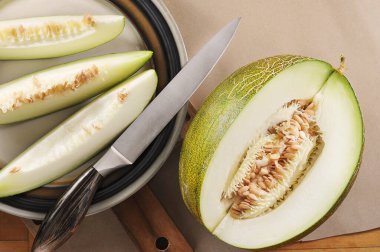 chopped melon, melon slices and a knife on craft paper background - top view flat view