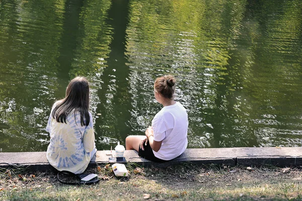 Two Girls Sitting Shore Pond Park — Zdjęcie stockowe
