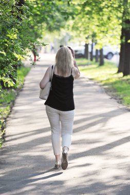 blonde walks down a spring alley - back view