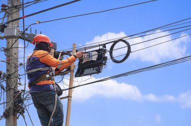 Ahşap merdivendeki teknisyenin düşük açılı görüntüsü mavi gökyüzüne karşı elektrik direğindeki internet dağıtıcı kutusuna fiber optik sistem kuruyor.