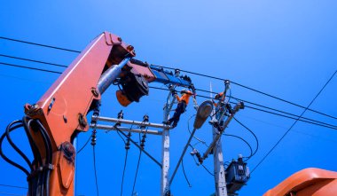Vinçli iki elektrikçinin düşük açılı görüntüsü mavi açık gökyüzü arkaplanına karşı elektrik iletimi yüklemeye çalışıyor 