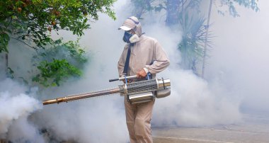 Sivrisinekleri ortadan kaldırmak ve kenar mahallelerde büyüyen dang hummasını önlemek için sis püskürtme makinesi kullanan açık hava sağlık çalışanı.