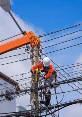 Vinç kamyonlu Asyalı elektrikçi dikey çerçevede mavi gökyüzüne elektrik direği ve kablo hatları kuruyor.
