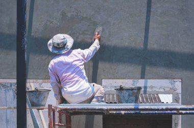 Asyalı inşaat işçisinin inşaat sahasında mala parlatma çimento duvarını kullanarak iskeledeki dikiz görüntüsü