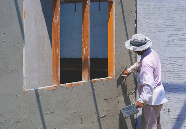 Asyalı inşaat işçisinin ev inşaatına beton duvar yapıştırmasının perspektif tarafı.