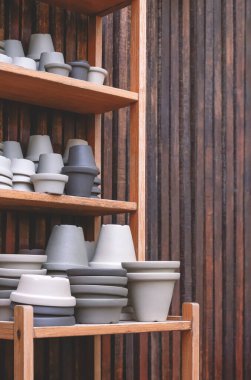 Dikey çerçeveli ahşap duvarlı ahşap rafta satılık gri terracotta saksıları grubu.