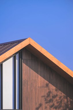 Güneş ışığı ve gölgesi, dikey çerçevede mavi gökyüzüne karşı yarasalar desenli eski ahşap çatı yüzeyinde.