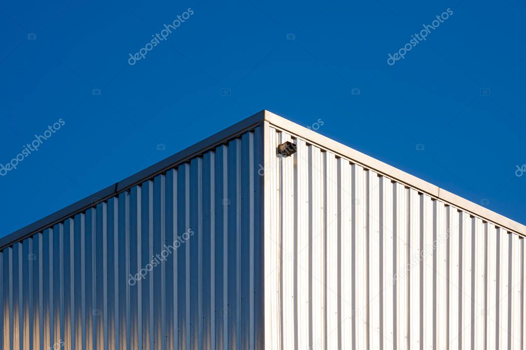 Sunlight reflection on surface of corrugated steel wall of warehouse building against blue clear sky background in symmetry and low angle view