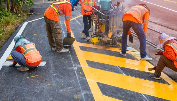 Termoplastik sprey işaretleme makineli yol işçileri grubu asfalt yoldaki sarı trafik işaretini boyuyor.