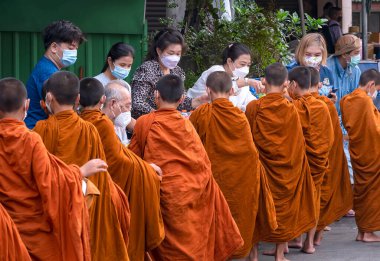 Samutsakhon, Tayland - 9 Mayıs 2022: Koruyucu maskeli insanlar sabah vakti Budist rahibelere yemek sunar