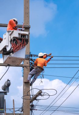 Elektrikçi grubu elektrik direğine elektrik sistemlerini dikey çerçevede mavi gökyüzü arkaplanına karşı yüklemeye çalışıyor