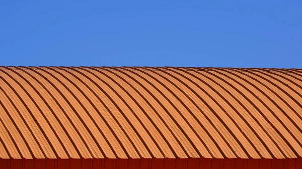 蓝天背景下橙色波纹钢制拱顶曲线图案 — 图库照片