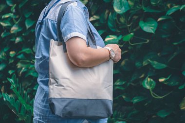 Bulanık yeşil bitki duvarı arka planında tekrar kullanılabilir tuval çevre dostu çanta taşıyan iri yarı bir kadının orta kısmı.