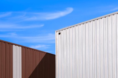 Low angle view of corrugated steel wall of 2 warehouse building against blue sky background in perspective side view