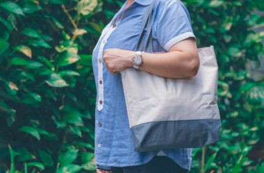 Midsection of plus size woman carrying reusable canvas eco friendly tote bag on blurred green plant wall background