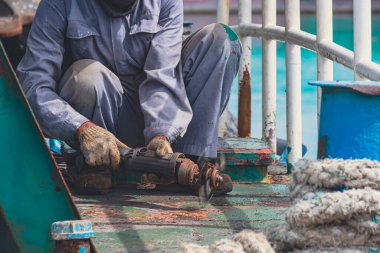 Cropped image of worker using electric steel cracker to cracking rusty stern floor of fishing boat, renovation and improvement concept
