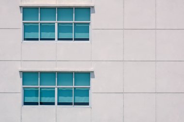 Two rows of glass windows with sun blinds on large square concrete tiles wall of office building