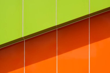 Sunlight and shadow on surface of vibrant green and orange aluminum composite tiles wall outside of modern building