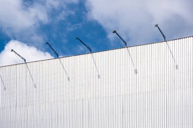 Outdoor corrugated steel advertising billboard structure with spotlights against white clouds on blue sky background, low angle view with copy space