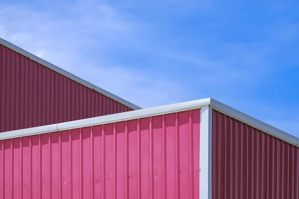 Minimal exterior architecture background of pink corrugated steel rooftop of industrial building against blue sky background