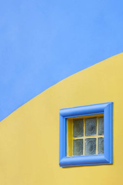 Minimal architecture background of small glass brick block fixed window on colorful blue and yellow vintage building wall in vertical frame