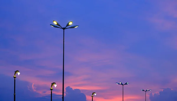 Silhouette row of modern street lights and retro street lamp posts in viewpoint area against sunset sky background