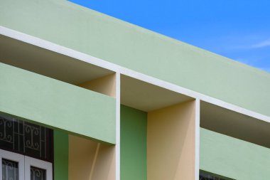 Modern yeşil ve bej bina duvarında mavi gökyüzü arka planına karşı gölgelendirme yüzgecinin soyut geometrik deseni