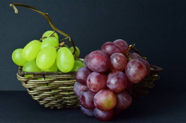 Kapatın. Üzüm çeşitliliği, hasır sepette kümeler ve koyu arkaplan.