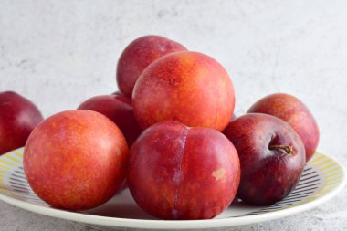 Yaklaş, porselen tabakta kırmızı erikler ve taş zemin. 