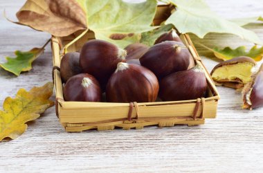 Masadaki küçük tepside kestaneler ve dağınık doğal yapraklar. Sonbahar.