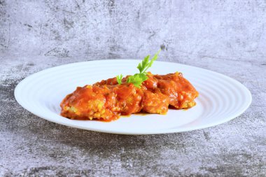 Beyaz bir tabakta servis edilen domates soslu, sarımsaklı ve maydanozlu morina balığı..