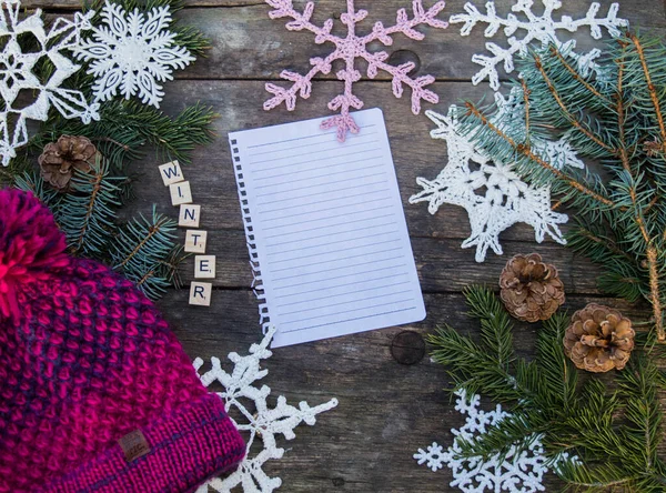 crochet snowflake ornaments on wooden ground with space for text and fir branch and cones and a knitted bobble hat background