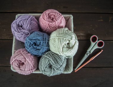 Pastel renkli yün toplar sepetin içinde makas ve el yapımı koyu kahverengi ahşap bir kancayla.