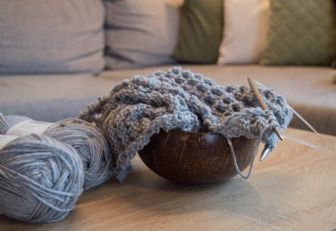 Ahşap bir kasede örgü iğneleri ve el yapımı bir eşarp olan gri renkli yün.