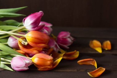 Koyu kahverengi ahşap zemin üzerinde pembe ve turuncu laleler.